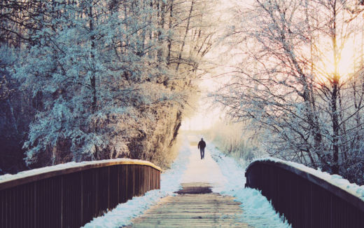 Brücke im Wald mit schneebedeckenten Bäumen, im Sonnenuntergang des Horizonts ein Mann.